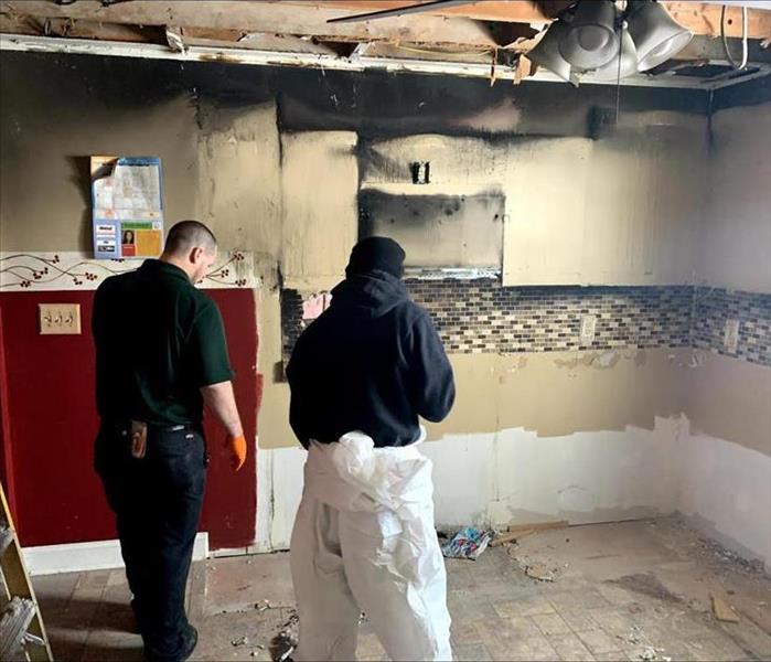 Two Servpro employees inspect a soot-covered kitchen.